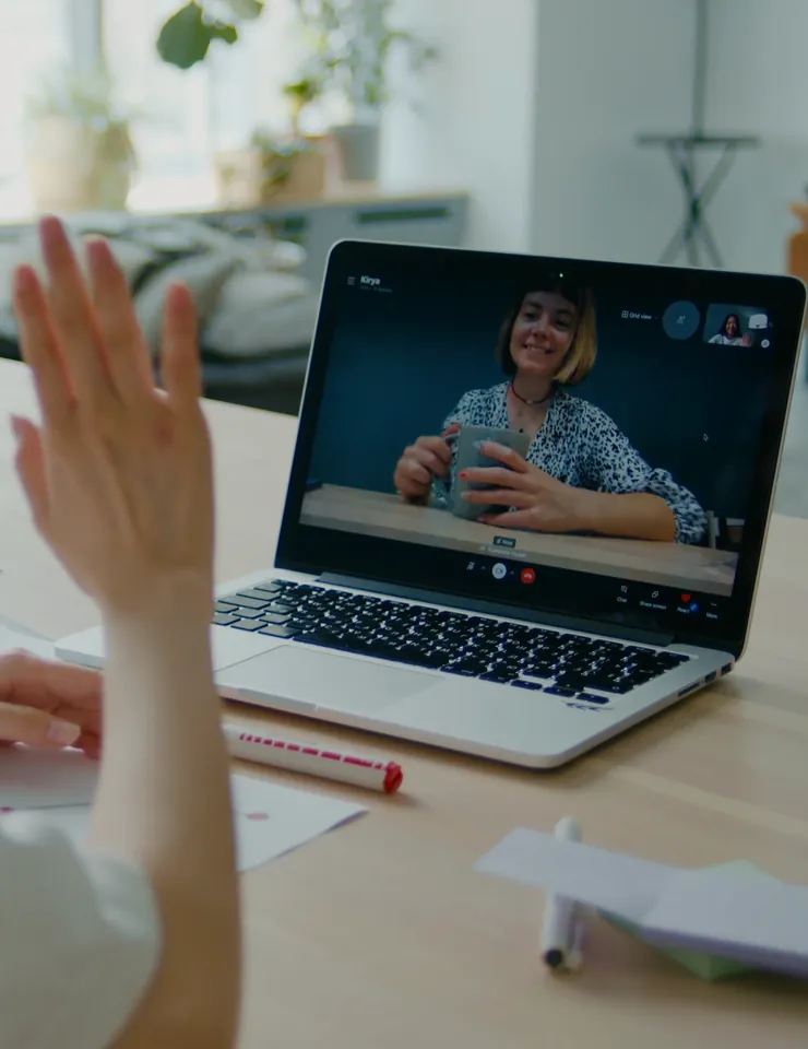 Adult waving during a video call with a mentor on a laptop